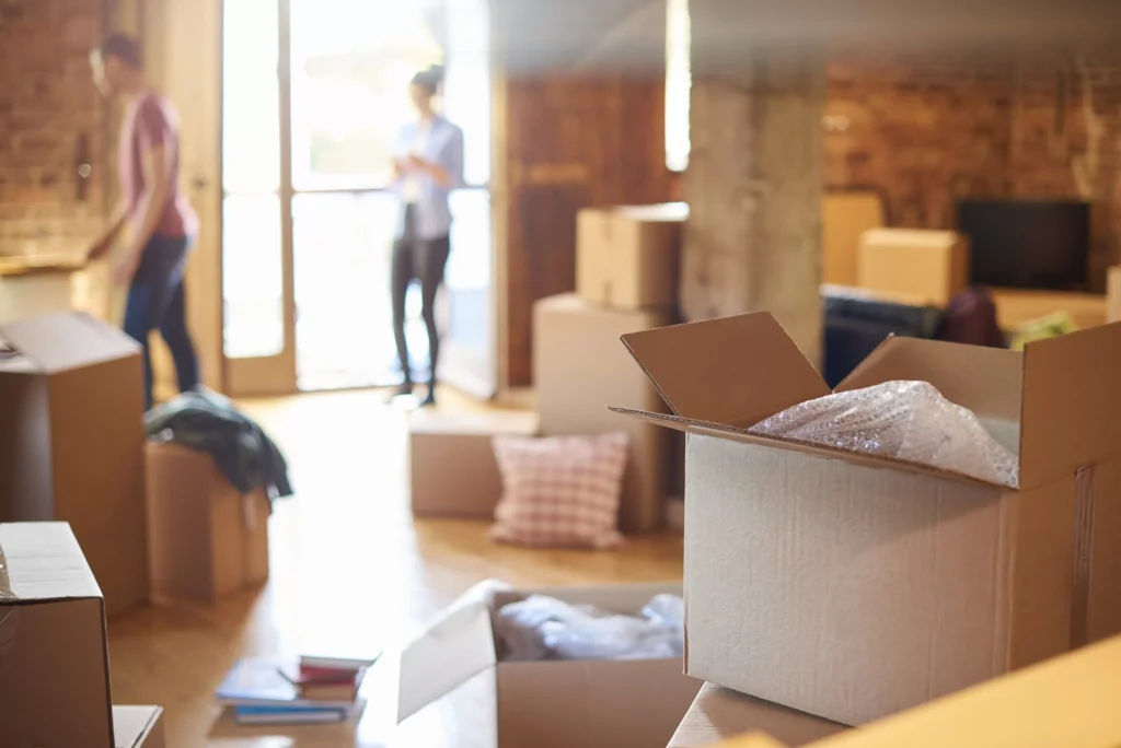 Open cardboard boxes and people preparing to move in a sunlit apartment.