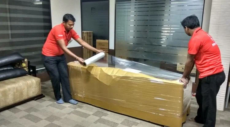 Two movers wrapping a sofa with protective plastic.