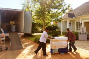 Movers loading a wrapped mattress onto a truck outside a house